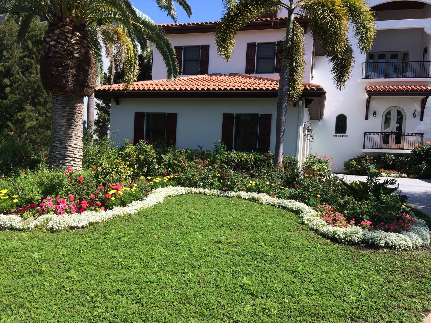 Stucco home with wrap-around white flowers and colored flowers behind